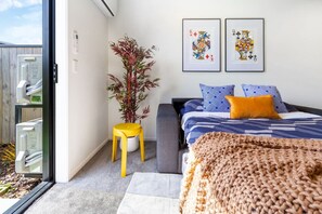 A bedroom with a bed, a potted plant, and two framed pictures on the wall.