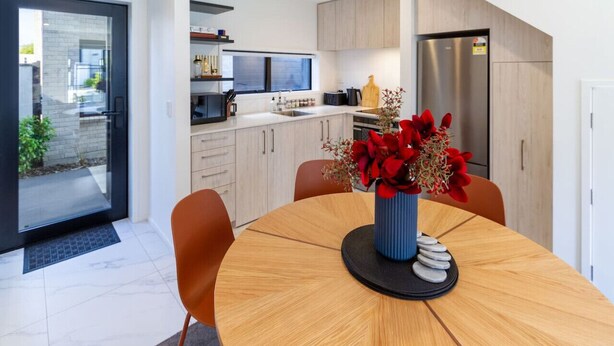 A modern kitchen with white cabinets, a stainless steel refrigerator, and a dining table with orange chairs. - Bright and Stylish 2BR Near Addington Park (Christchurch)