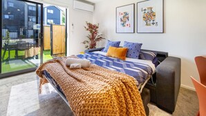A bedroom with a bed, a sofa, a chair, and a large window. - Bright and Stylish 2BR Near Addington Park (Christchurch)