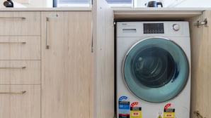 Uma lavanderia compacta e moderna, com máquina de lavar e secadora frontais, armários de madeira e classificação de eficiência energética.