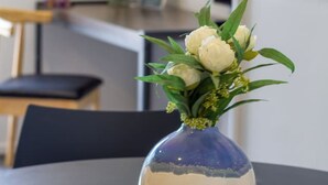 A vase with white flowers on a table in a room with a TV and a framed picture on the wall.