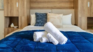 A hotel room with a large bed, a blue quilted bedspread, and a wooden headboard.