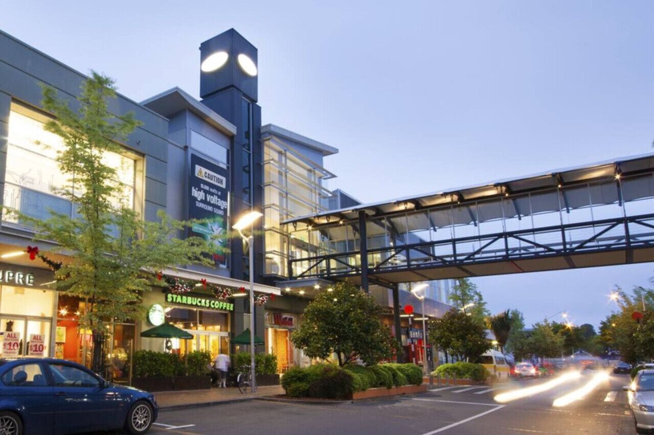 A modern building with a Starbucks coffee shop, a pedestrian bridge, and a parking lot with cars.