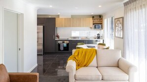Ein modernes Wohnzimmer mit einer Couch und einem Couchtisch, im Hintergrund eine Küche und ein Essbereich mit Tisch und Stühlen.