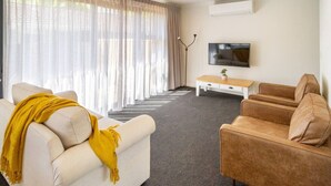 Ein Wohnzimmer mit einem beigen Sofa, einem braunen Sofa, einem Couchtisch und einem an der Wand montierten Fernseher.