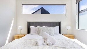 Ein modernes Schlafzimmer mit einem großen Bett, zwei Nachttischen und einem Fenster mit Blick auf ein Gebäude.