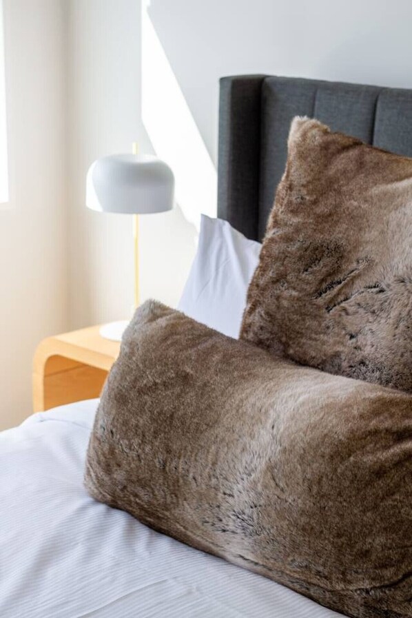 A bed with two brown pillows, a white pillow, and a wooden nightstand with a lamp.