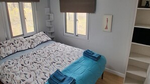 Ein Schlafzimmer mit Bett, zwei Fenstern, einem Regal und einer Tür.