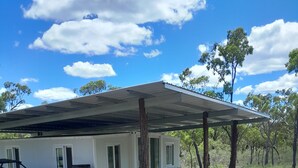 Ein modernes Haus mit überdachter Veranda, einem Fahrzeug und einer natürlichen Landschaft.