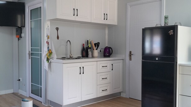Eine moderne Küche mit weißen Schränken, einem schwarzen Kühlschrank und einem grauen Teppich mit Muster.