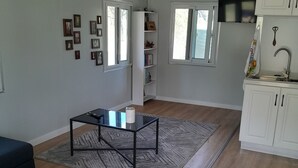 Ein stilvolles Wohnzimmer mit einer Couch, einem Couchtisch und einem Teppich. An den Wänden hängen gerahmte Bilder und ein Bücherregal mit Büchern und Dekorationsobjekten.