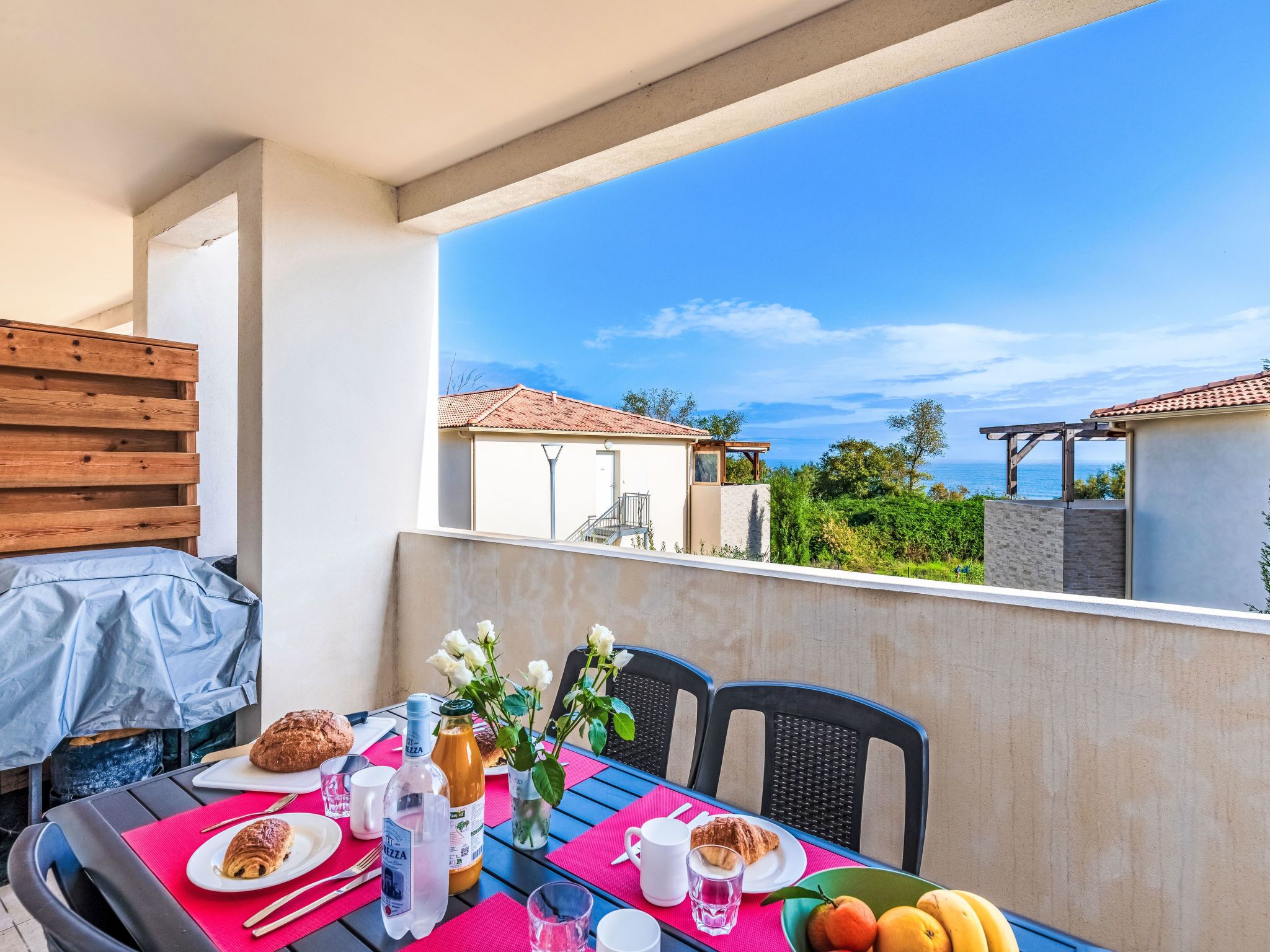 A balcony with a table set for breakfast, including croissants, a bottle of water, and a glass of juice.
