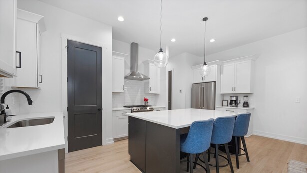 A modern kitchen with white cabinetry, a central island with bar stools, stainless steel appliances, and pendant lighting. - Sleeps 10. Near NODA, Plaza, Uptown. Pet Friendly. Fenced Yard + Firepit (Charlotte)