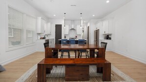 A modern kitchen with white cabinets, a wooden dining table, and blue chairs. - Sleeps 10. Near NODA, Plaza, Uptown. Pet Friendly. Fenced Yard + Firepit (Charlotte)