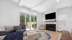 A modern living room with a sofa, a coffee table, a fireplace, and a television mounted on the wall. - Sleeps 10. Near NODA, Plaza, Uptown. Pet Friendly. Fenced Yard + Firepit (Charlotte)