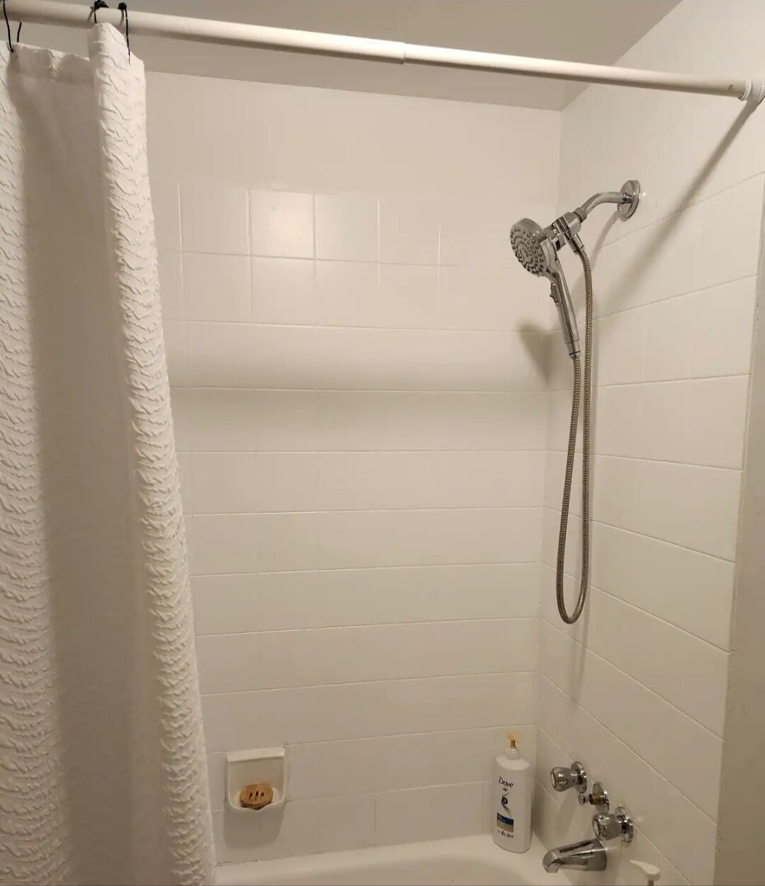 A shower area with a handheld showerhead, a towel rack, and a bottle of Dove body wash.