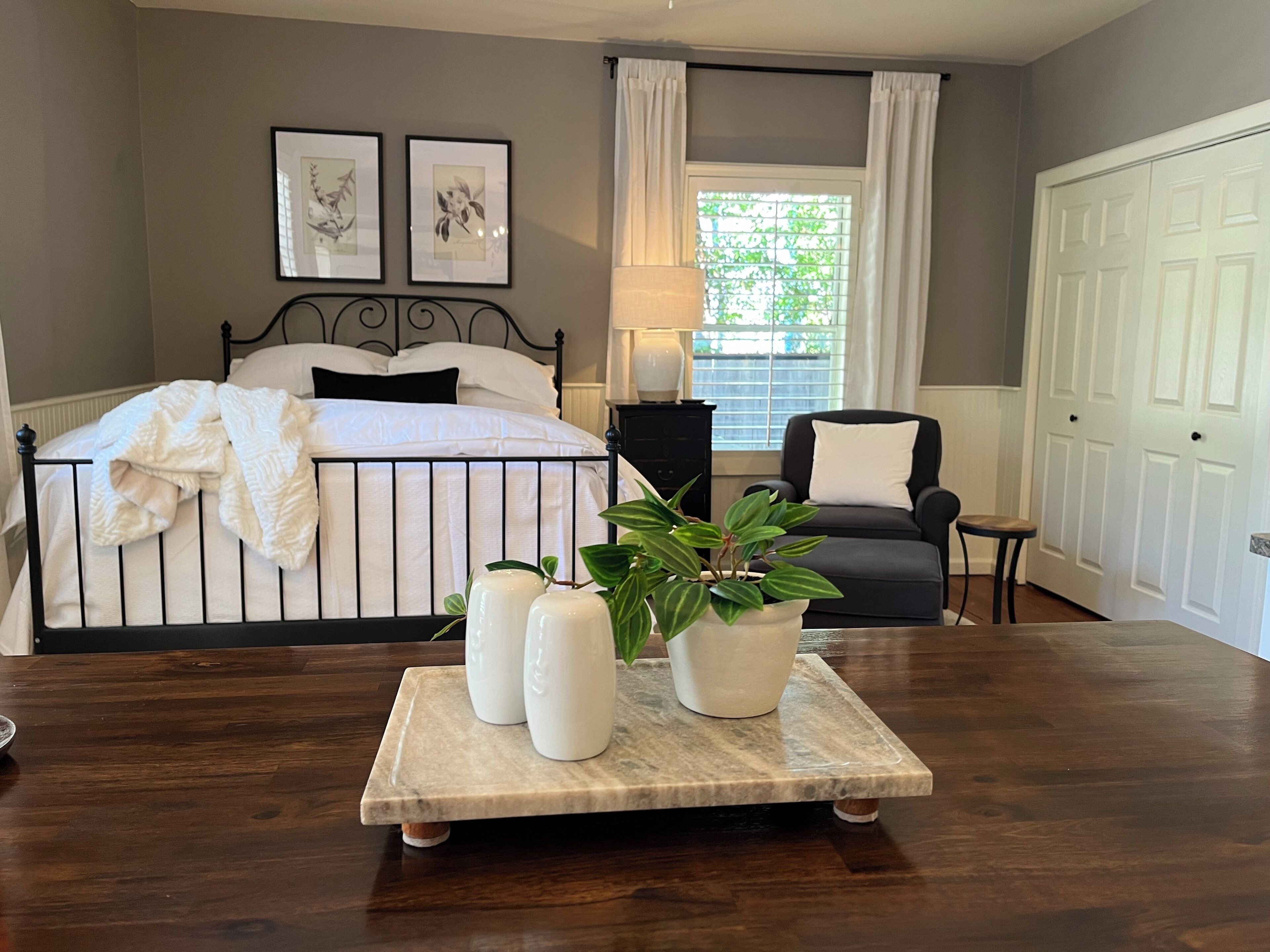 A bedroom with a bed, a nightstand, a chair, a window with curtains, and a door.