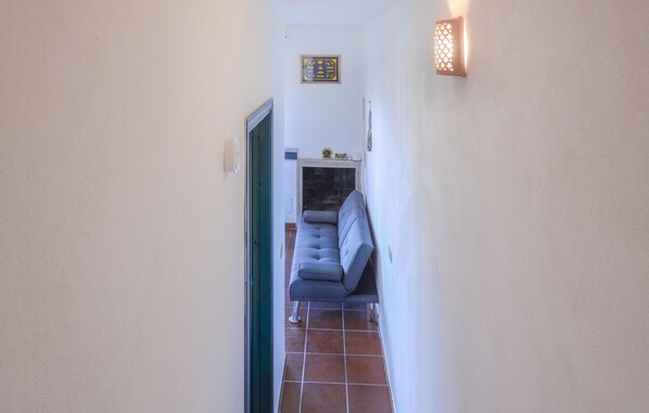 A narrow hallway with a grey sofa against the wall, a small shelf with decorative items, and a framed picture above the sofa.