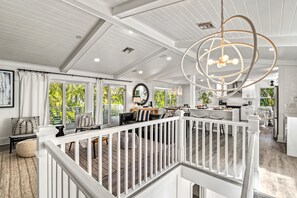 Un vaste espace de vie agrémenté d’une balustrade blanche, un coin repas et une cuisine avec des meubles blancs.