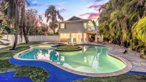 A modern house with a swimming pool, surrounded by palm trees and a well-maintained lawn.