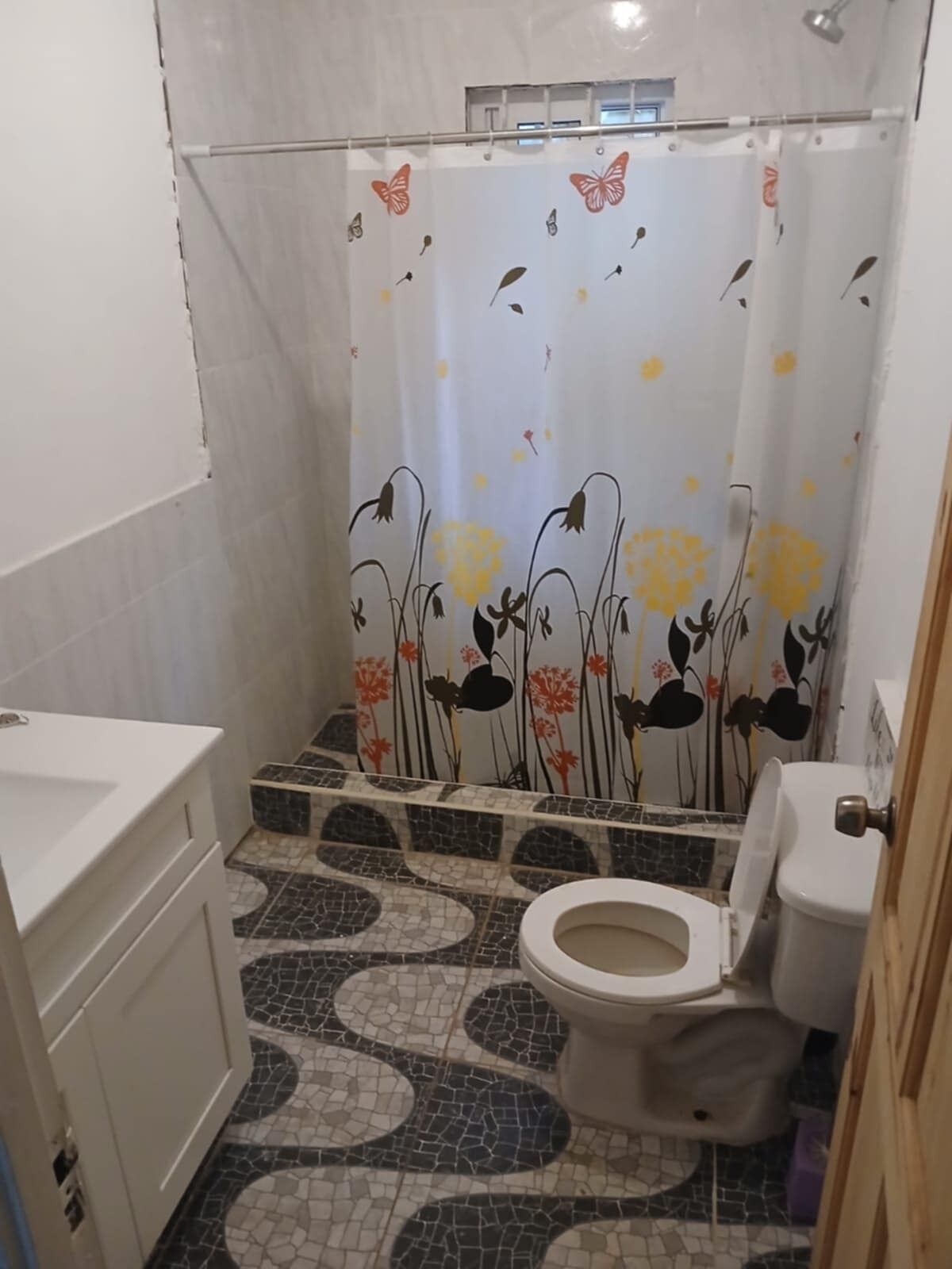 A bathroom with a toilet, a sink, and a shower curtain with floral and butterfly designs.