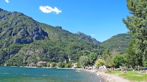 A lakeside view with a beach, mountains, and a few buildings in the background. - Francesca by Interhome (Porlezza)