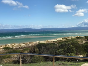 A coastal landscape with a beach, grassy dunes, and a clear sky.