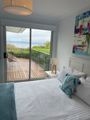 Une chambre avec un grand lit, une table de chevet, une lampe et une vue sur un balcon équipé d’une chaise.