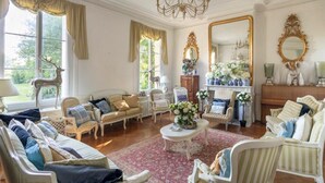 Uma sala de estar ampla com um lustre, vários espaços de estar e grandes janelas.