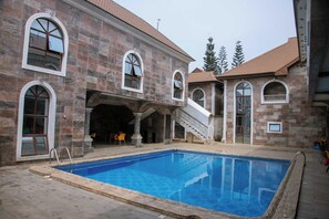 A stone building with a swimming pool, outdoor seating, and a staircase leading to an upper level. - Jacobs Place Hotel (Owerri)