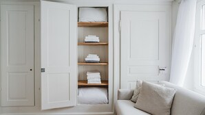 A room with a built-in wardrobe featuring multiple shelves for storage, a light-colored sofa with a cushion, and a wooden floor. - Blueground | Oberstrass, rooftop, a/c, equipped (Zurich)