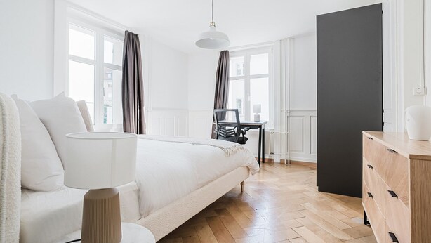 Ein modernes Schlafzimmer mit einem großen Bett, Nachttisch, Lampe und Schreibtisch mit Stuhl.