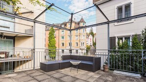 Eine Dachterrasse mit Sitzgelegenheit, einem Blumentopf und Blick auf umliegende Gebäude.