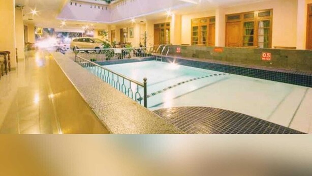 Une piscine avec une terrasse carrelée, un espace couvert doté d’un toit et une voiture garée à l’extérieur.