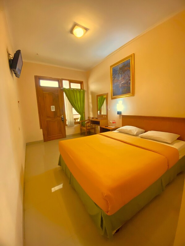 A hotel room with a large bed, a television mounted on the wall, and a painting above the bed.