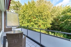 Un balcon doté de meubles en osier et d’une table, offrant une vue sur une zone verdoyante et densément boisée.