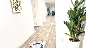 Een gang met houten vloeren, een zwart-wit tapijt, een potplant en een lijst met een foto aan de muur.
