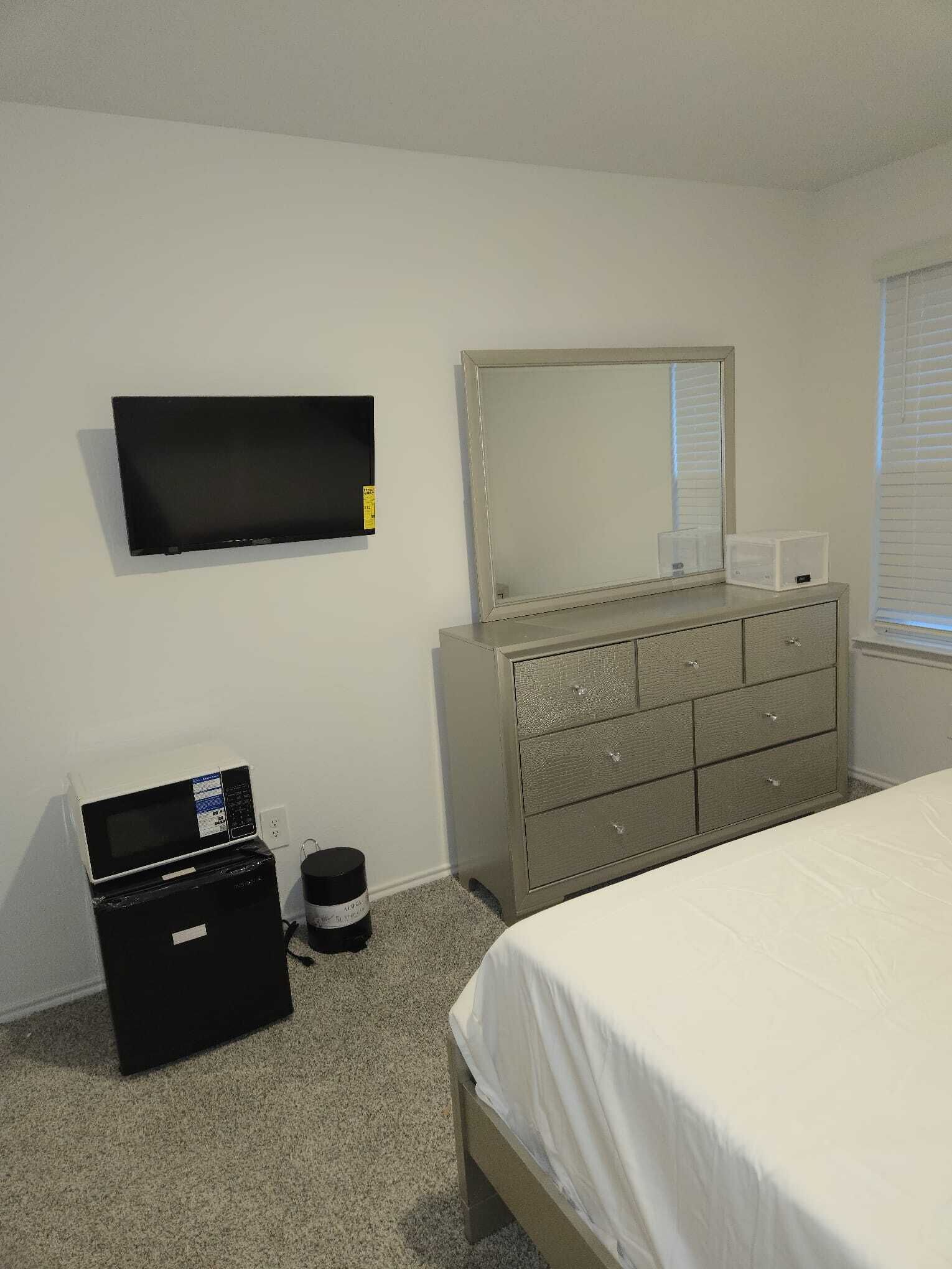 A bedroom with a bed, dresser, television, and a microwave.