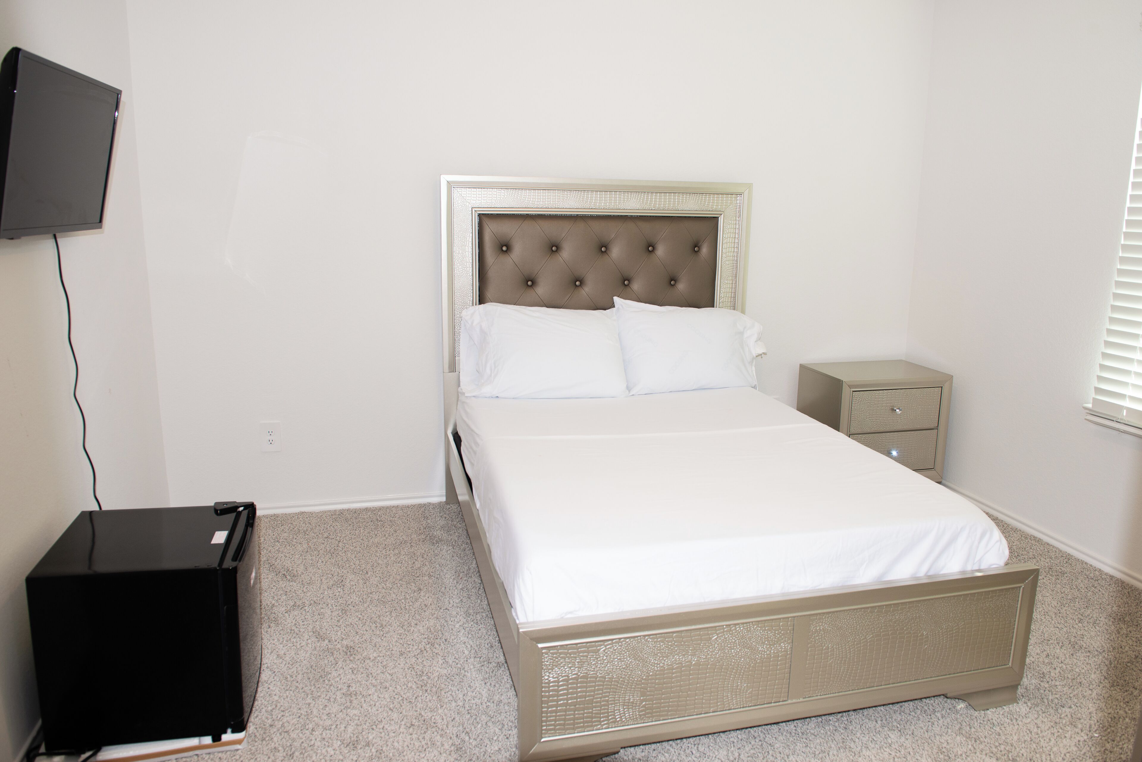 A bedroom with a bed, a nightstand, a television mounted on the wall, and a small black object on the floor.