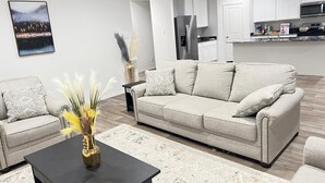 Een moderne woonkamer met een grijze bank, een zwarte salontafel en decoratieve planten.
