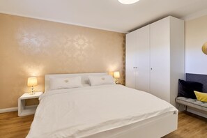 Quarto com uma cama grande, duas mesas de cabeceira com luminárias, um guarda-roupa e um sofá com almofadas.