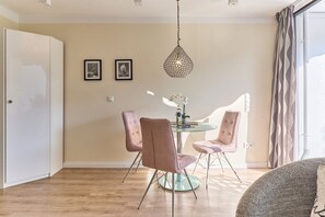 Uma sala de jantar com uma mesa redonda de vidro, duas cadeiras cor-de-rosa, um lustre e duas imagens emolduradas na parede.