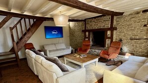 A cozy living room with a stone wall, a fireplace, a television, and a staircase. - Chouette and Hibou 30pers 2 Cottage : jacuzzi (Quibou)