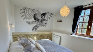 A bedroom with a bed, a wall mural of an owl, a hanging light fixture, and a window with curtains. - Chouette and Hibou 30pers 2 Cottage : jacuzzi (Quibou)