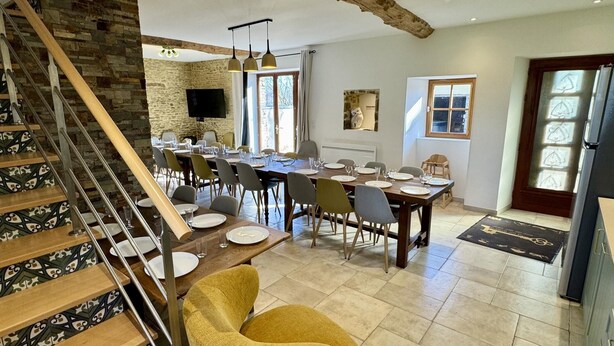 A dining area with a long table set for a meal, a staircase with patterned steps, and a rustic stone wall. - Chouette and Hibou 30pers 2 Cottage : jacuzzi (Quibou)