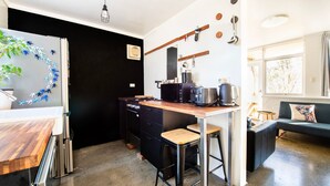 Cocina compacta con encimera de madera, electrodomésticos negros y un pequeño comedor con taburetes.
