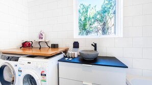 Una cocina funcional con lavadora, plancha pequeña y ventana con vista tropical.