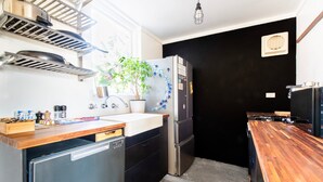 Cocina pequeña con lavabo, estufa y refrigerador. Se ve una ventana con una planta y una pared negra.
