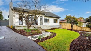 Une maison de plain-pied avec un jardin devant, une allée et une clôture en bois.