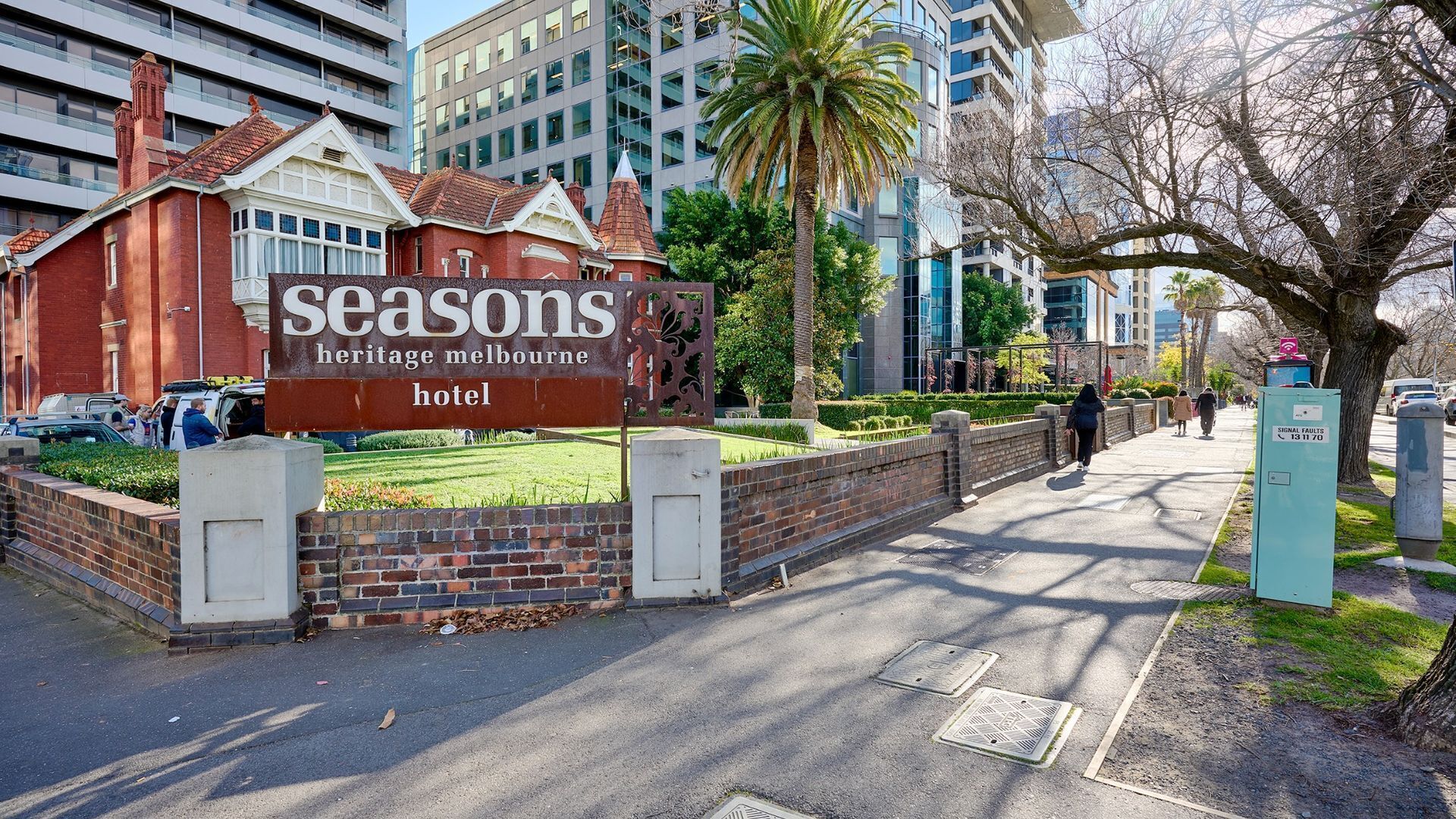 A Seasons Heritage Melbourne hotel sign with a brick wall and a pathway leading to the entrance.